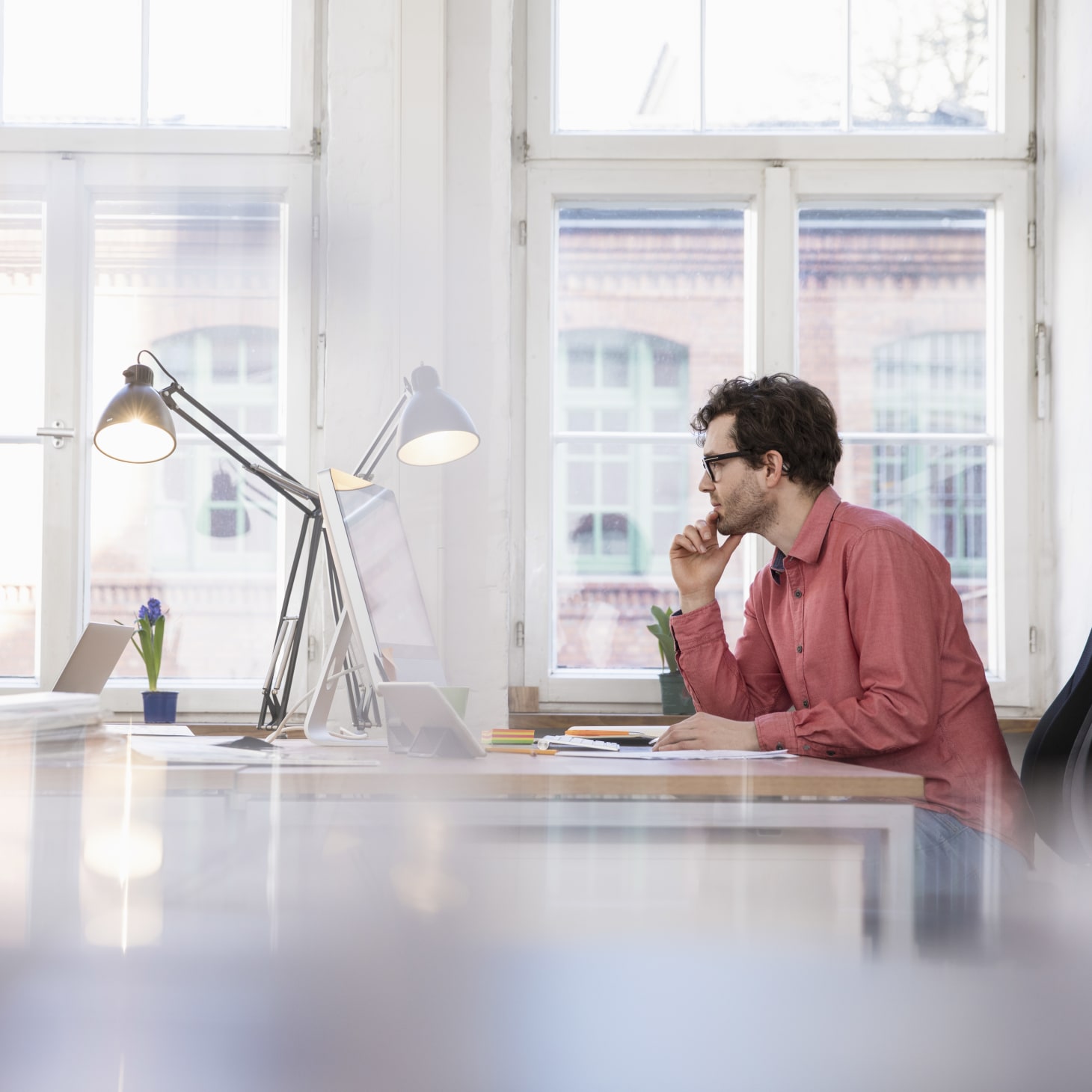 white man contemplating at his desk, in front of a window