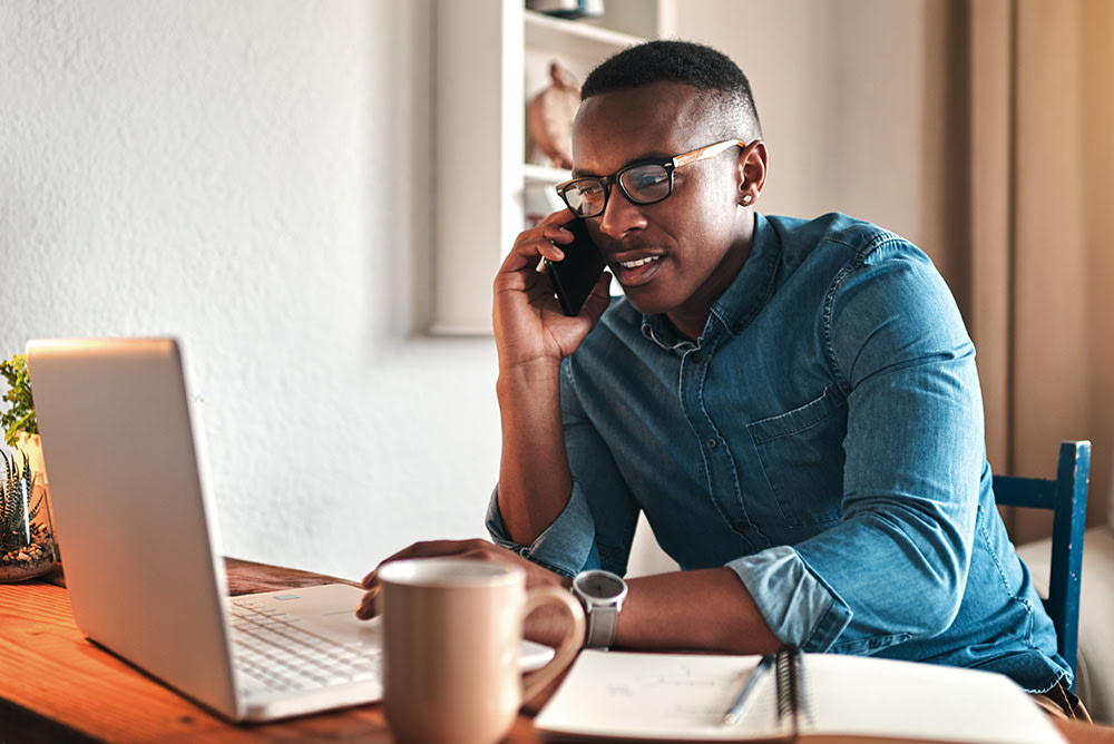 person on the phone working from laptop at home desk