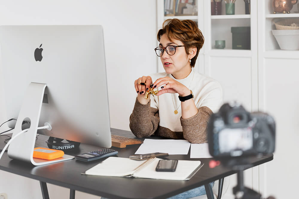 woman with short brown hair and glasses, working at a home desktop 